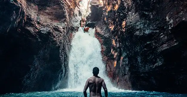 Un homme debout dans l'eau devant une cascade.