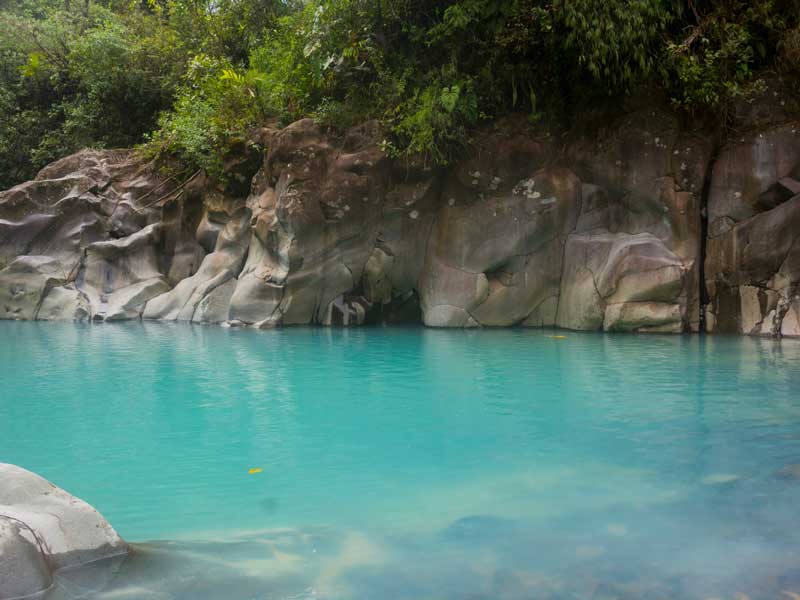 Un bassin d'eau bleue entouré de rochers et d'arbres.