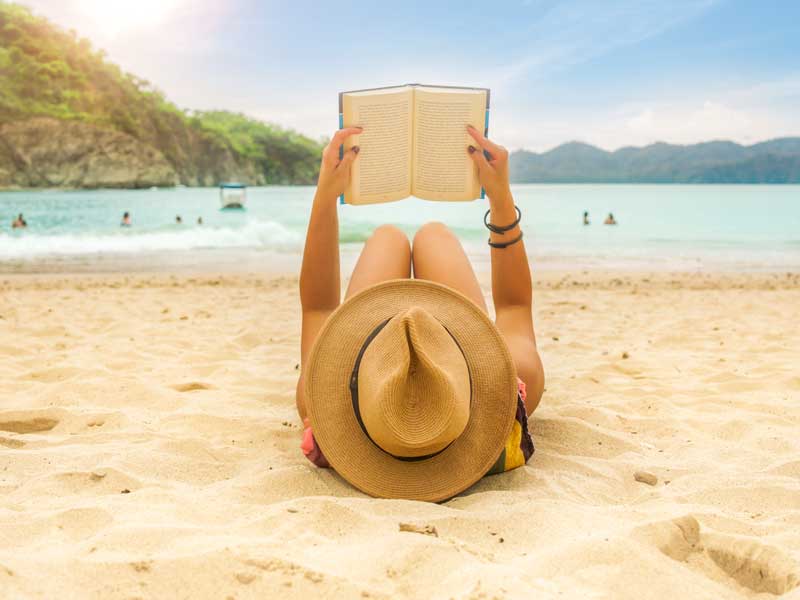 Une femme allongée sur la plage lisant un livre.