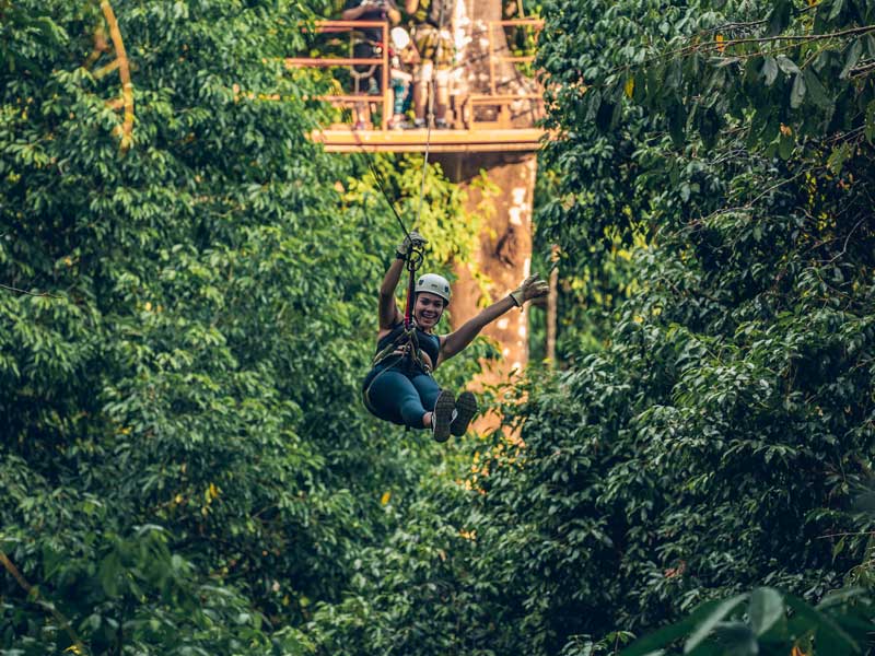 Une femme sur une tyrolienne au milieu d'une forêt.
