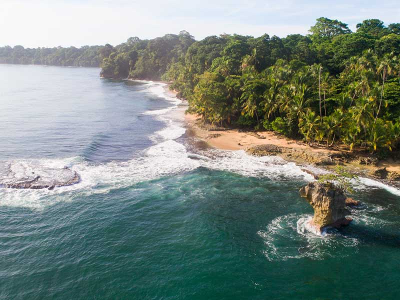 Vue aérienne d'une plage avec un rocher au milieu de l'océan.