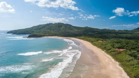 Vue aérienne d'une plage de sable située sur la côte pacifique d'Costa Rica, bordée d'eaux turquoise et de collines verdoyantes.