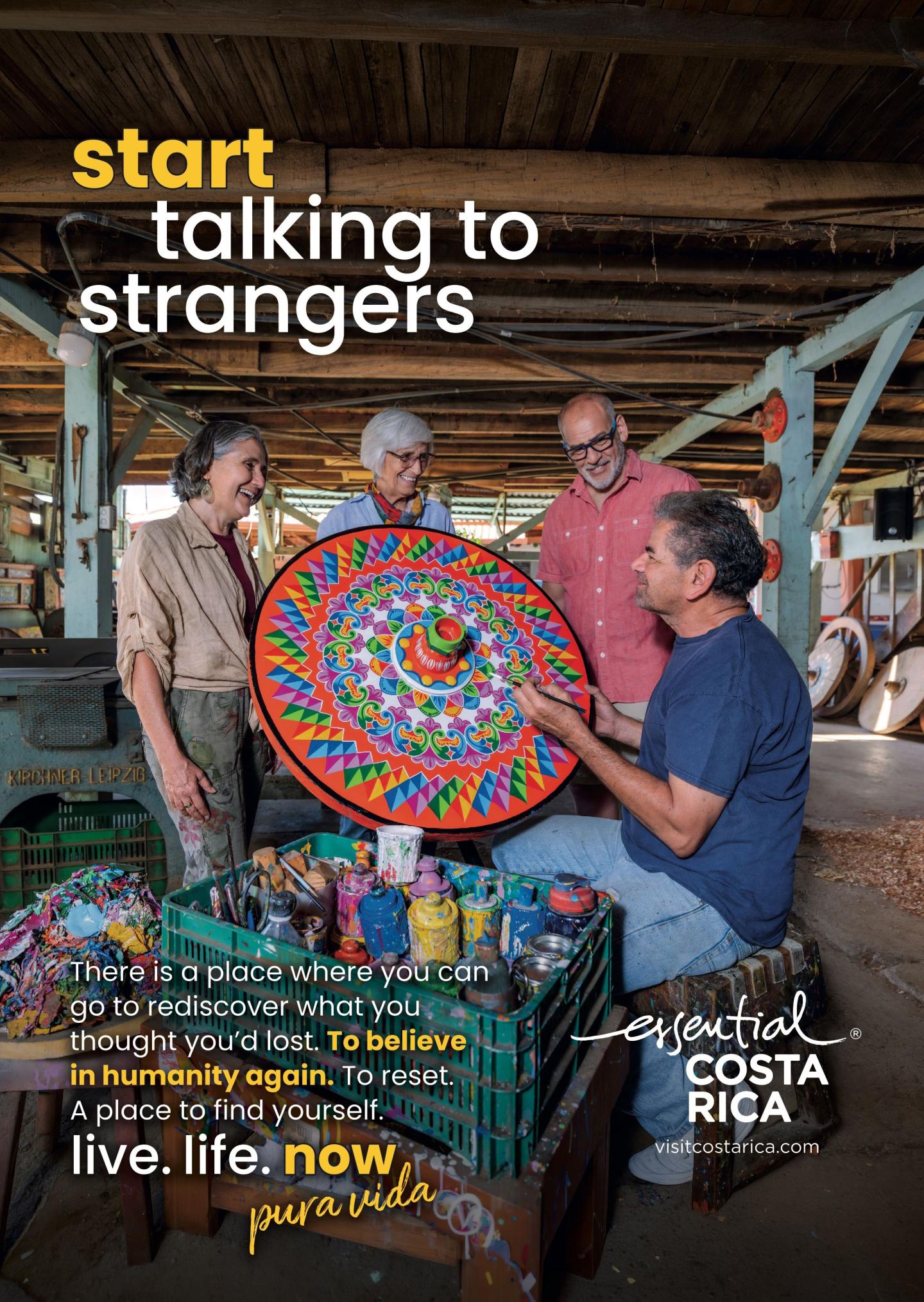 Publicité montrant quatre personnes dans un atelier en train de discuter avec un artisan tenant une grande pièce artisanale circulaire aux couleurs vives. Titre : « Commencez à parler à des inconnus ». Marque : « esencial Costa Rica, visitcostarica.com.