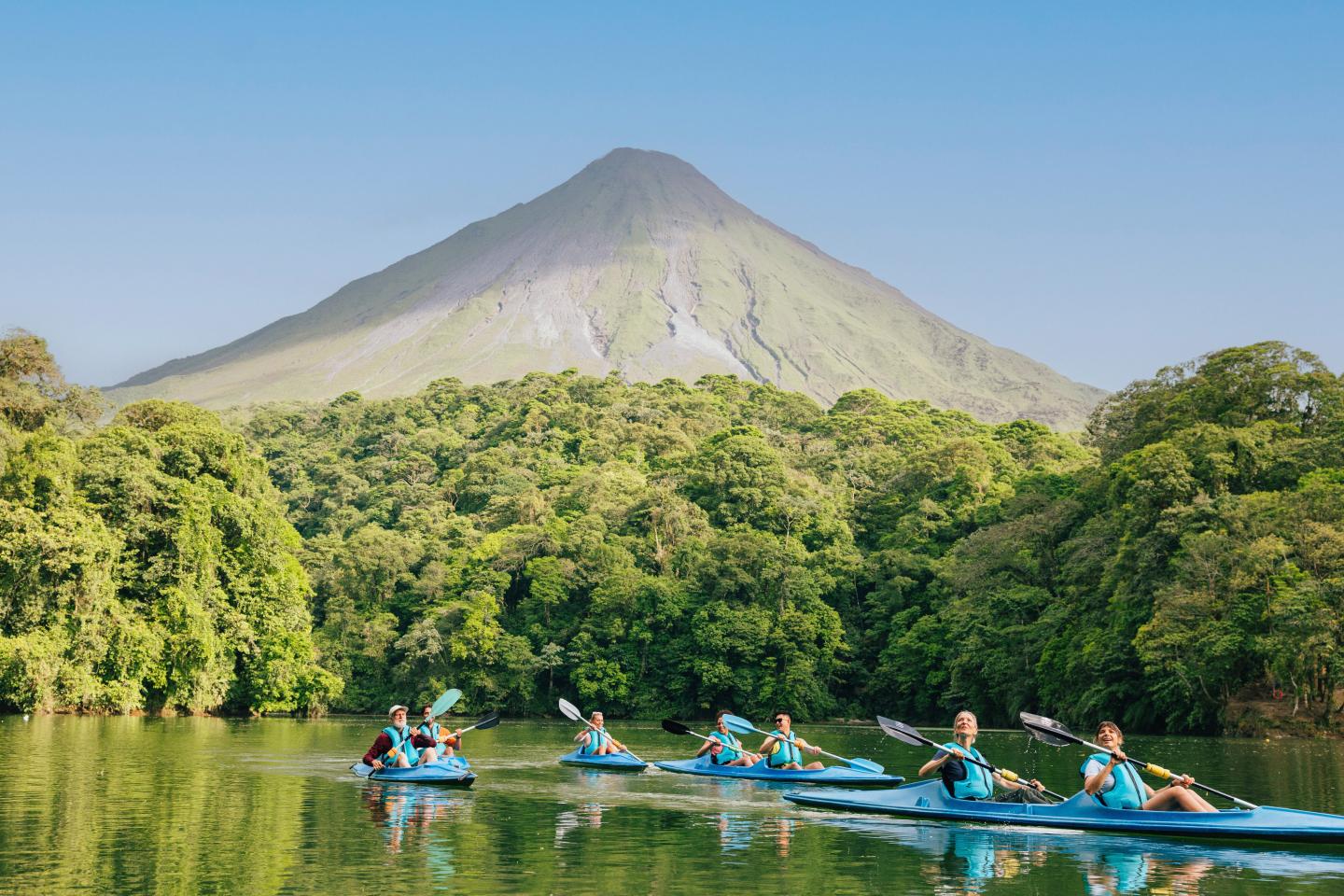 Sortie de kayak en groupe sur un lac paisible bordé de forêt tropicale, avec le volcan Arenal qui se profile en arrière-plan.